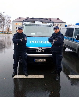 dwaj umundurowani policjanci stoją przed radiowozem
