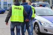 dwaj policjanci w żółtych kamizelkach prowadzą zatrzymanego
