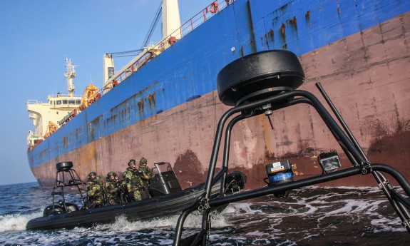Łódka z policyjnymi kontrterrorystami podpływa do burty dużego statku towarowego.