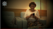 starsza pani siedzi na kanapie i w ręku trzyma telefon komórkowy