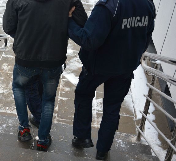 Policjant prowadzi mężczyznę, który ma skute nogi