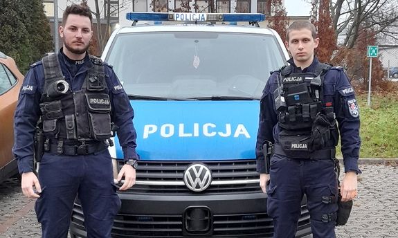 dwaj umundurowani policjanci stojący przy radiowozie