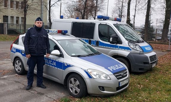 umundurowany policjant stoi przy dwóch radiowozach