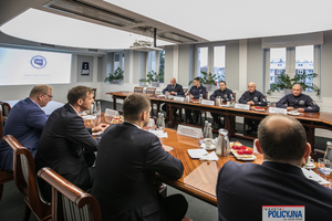 tyłem do fotografa za stołem siedzą czterej mężczyźni w garniturach, na przeciwko nich czterej umundurowani oficerowie Policji i mężczyzna w garniturze. Z lewej strony widać rzucone na ekran logo CBZC