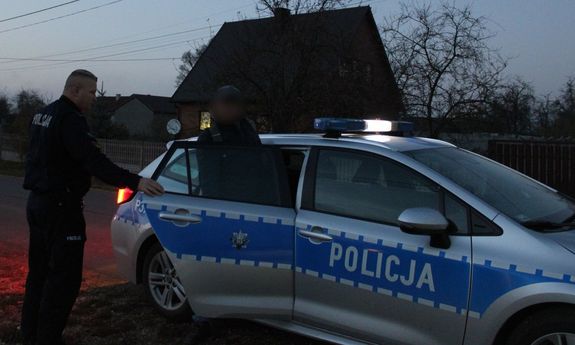 radiowóz oraz policjant, który otwiera tylne drzwi radiowozu. Z radiowozu wychodzi mężczyzna