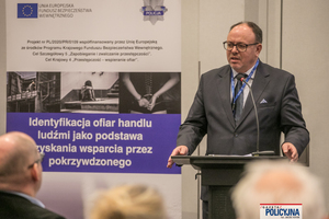 prelegent w garniturze przemawia do zebranych na sali