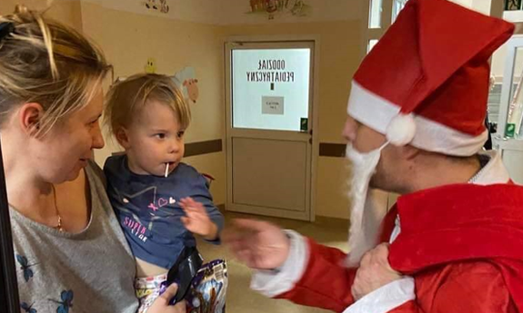 Mikołaj wręcza dziecku trzymanemu na rękach przez kobietę prezent