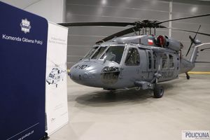 na pierwszym planie ścianka prasowa Komendy Głównej Policji, w tle śmigłowce typu S-70i Black Hawk