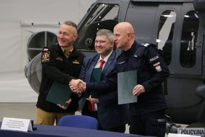 Komendant Główny Państwowej Straży Pożarnej składa uścisk dłoni Komendantowi Głównemu Policji, po środku stoi mężczyzna w garniturze