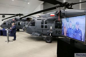 mężczyzna przemawia na mównicy, w tle stoją dwa śmigłowce typu S-70i Black Hawk