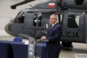 mężczyzna w garniturze przemawia na mównicy, w tle stoi śmigłowiec typu S-70i Black Hawk