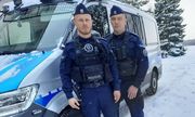 dwaj umundurowani policjanci biorący udział w akcji ratunkowej stoją przy radiowozie