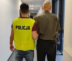 policjant w żółtej kamizelce z napisem Policja prowadzi zatrzymanego