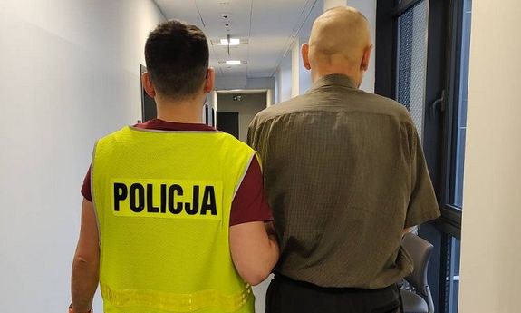 policjant w żółtej kamizelce z napisem Policja prowadzi zatrzymanego