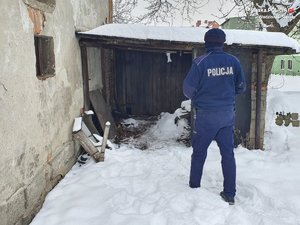 policjant podchodzi do prowizorycznej dobudówki, na ziemi leży śnieg