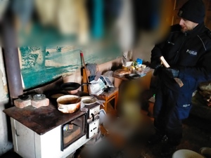 policjant w pomieszczeniu, w którym widać kuchenkę i stare garnki