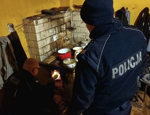 policjant rozpala ogień w piecu, obok stoi drugi policjant