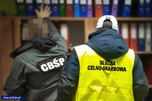 zdjęcie ilustracyjne - funkcjonariusz Centralnego Biura Śledczego Policji i Służby Celno - Skarbowej obok regału z segregatorami