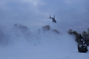 Policyjny śmigłowiec unoszący tumany śniegu z lądowiska.