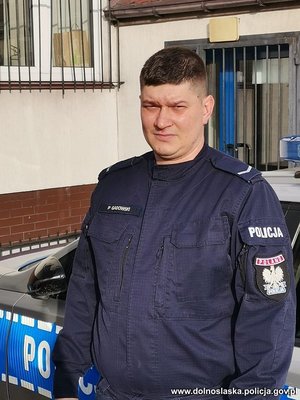 policjant przy radiowozie, w tle budynek komendy