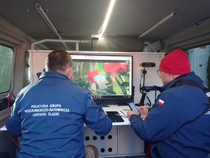 Zdjęcia przedstawiają dwóch policjantów podczas czynności poszukiwawczych przed ekranem komputera w pojeździe służbowym