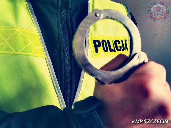 policjant w żółtej kamizelce trzymający w dłoni kajdanki