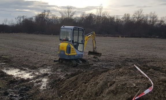 Stojąca na polu uprawnym koparka, w miejscu wykonywania prac ziemnych