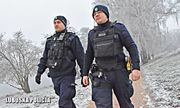 dwaj umundurowani policjanci w zimowej scenerii idą leśną drogą