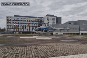 Policyjny helikopter na przyszpitalnym lądowisku, w tle budynek szpitala.