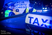 policjant i funkcjonariusz innej służby stoją przy kontrolowanej taksówce, za nimi widać radiowóz