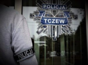 funkcjonariusz stoi na tle drzwi wejściowych do jednostki policji