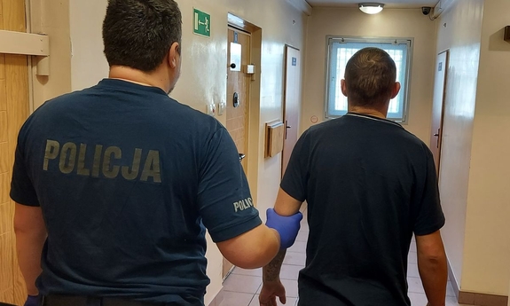 policjant prowadzi zatrzymanego mężczyznę przez korytarz