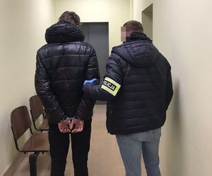 policjant prowadzi korytarzem zatrzymanego - widok z tyłu