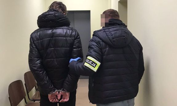 policjant prowadzi korytarzem zatrzymanego - widok z tyłu