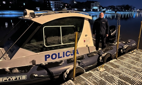 Policjant Komisariatu Wodnego Policji w Krakowie asp. szt. Rafał Zakrocki na tle łodzi służbowej