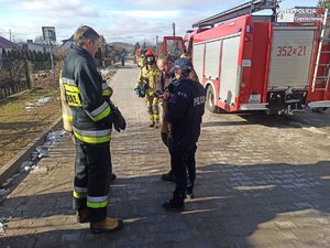 na zdjęciu policjantka rozmawia ze strażakami, w tle woź strażacki