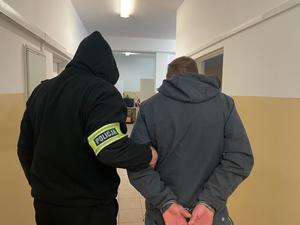 Złodziej rowerów prowadzony korytarzem przez policjanta, który ma na ramieniu żółta opaskę  z czarnym napisem Policja