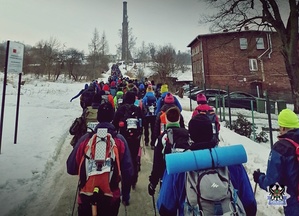 na dworze ludzie w zimowych ubraniach i z plecakami idący po drodze, wokół zaśnieżony krajobraz