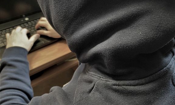 Mężczyzna w kapturze siedzący przy komputerze