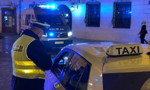 Umundurowany policjant kontroluje kierowcę taksówki w centrum Lublina. z tyłu widać policyjny radiowóz