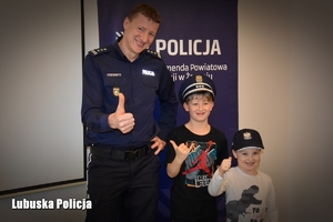 umundurowany policjant pozuje do zdjęcia z dziećmi na tle ścianki policyjnej