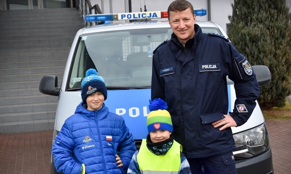 umundurowany policjant pozuje do zdjęcia na tle radiowozu z dziećmi