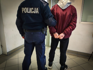 Policjant trzyma mężczyznę w kajdankach za ramię
