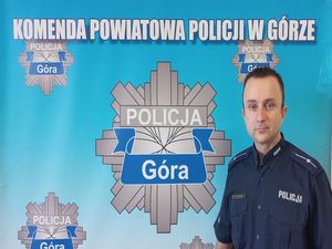 policjant w mundurze na tle niebieskiej planszy z napisem Komenda Powiatowa Policji w Górze oraz gwiazdą policyjną
