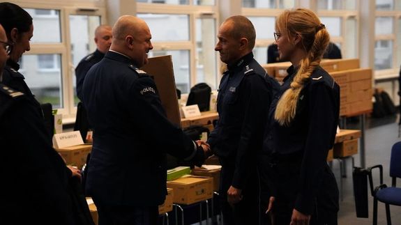 Podczas uroczystości Komendant Wojewódzki Policji w Gdańsku ściska dłoń stojącemu przed nim policjantowi, wokół stoją inni funkcjonariusze