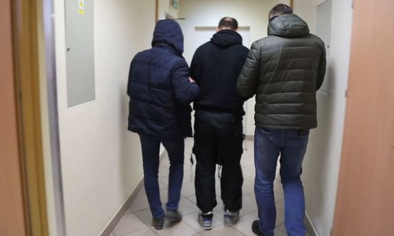 dwaj policjanci w cywilnych ubraniach prowadza korytarzem zatrzymanego mężczyznę