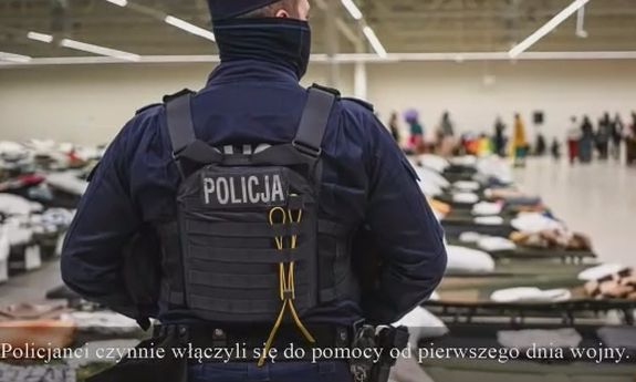 umundurowany policjant zwrócony przodem do sali na której ustawione są łóżka dla uchodźców z Ukrainy - widok z tyłu