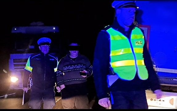 umundurowani policjanci ruchu drogowego w odblaskowych kamizelkach prowadzą kierowcę zestawu ciężarowego