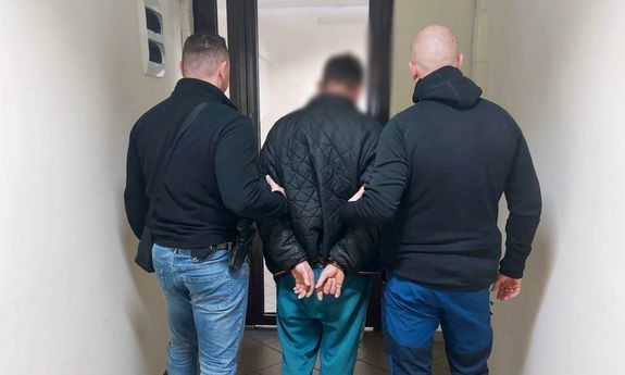 dwaj ubrani po cywilnemu policjanci prowadzą zatrzymanego - widok z tyłu