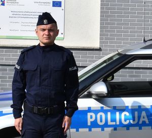 umundurowany policjant pozuj do zdjęcia na tle radiowozu